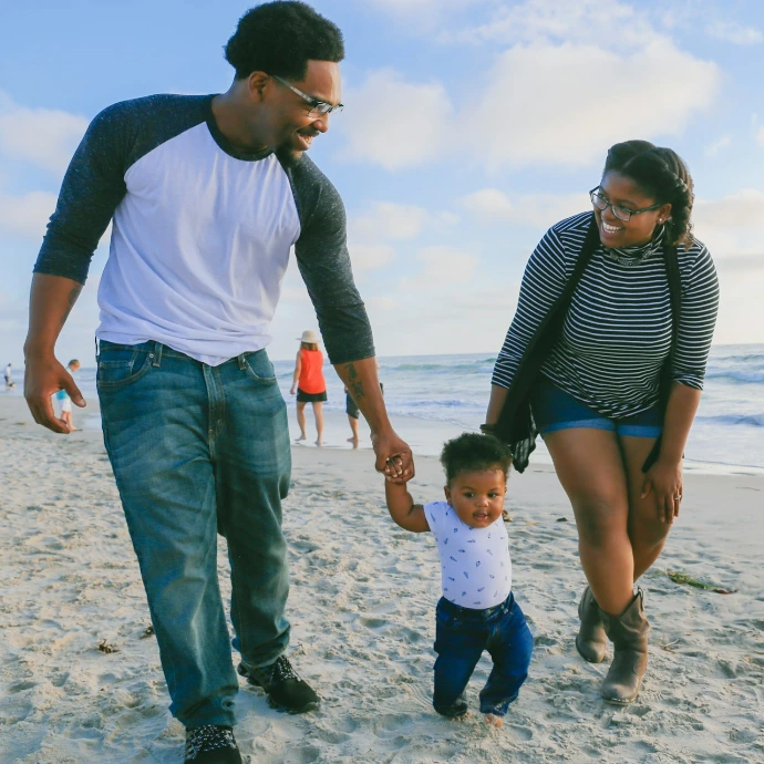 man in black and white striped long sleeve shirt holding baby in white shirt on beach